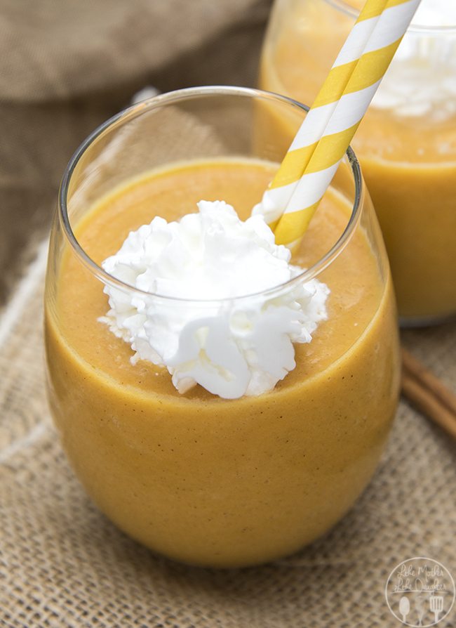Angled view of a pumpkin pie smoothie in a glass with straws and whipped cream.