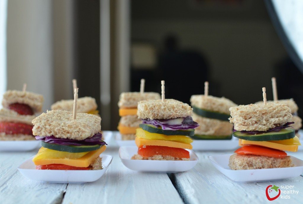 Multiple kids sandwiches on little white plates on a table.