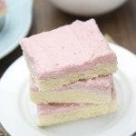 Angled view of strawberry frosted sugar cookie bars stacked on a white plate.