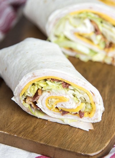 A close up of a turkey bacon ranch wrap on a piece of wood.