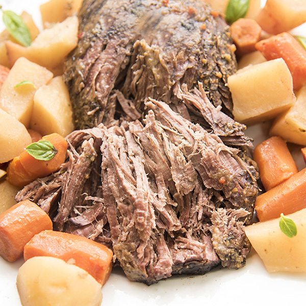 A beef roast on a plate surrounded by carrots and potatoes.