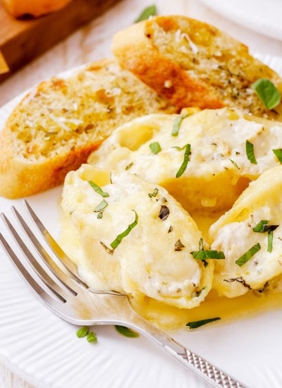 A plate of alfredo stuffed shells and garlic bread pieces.