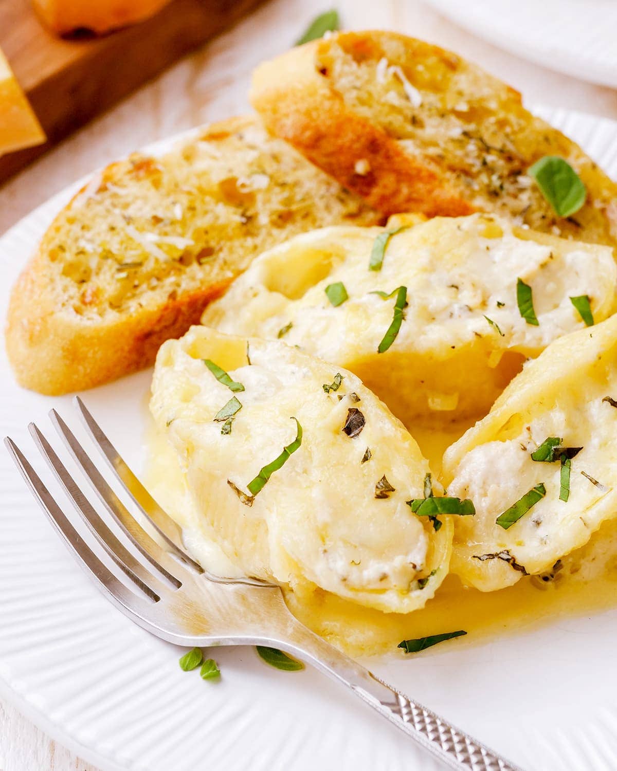 A plate of alfredo stuffed shells and garlic bread pieces.