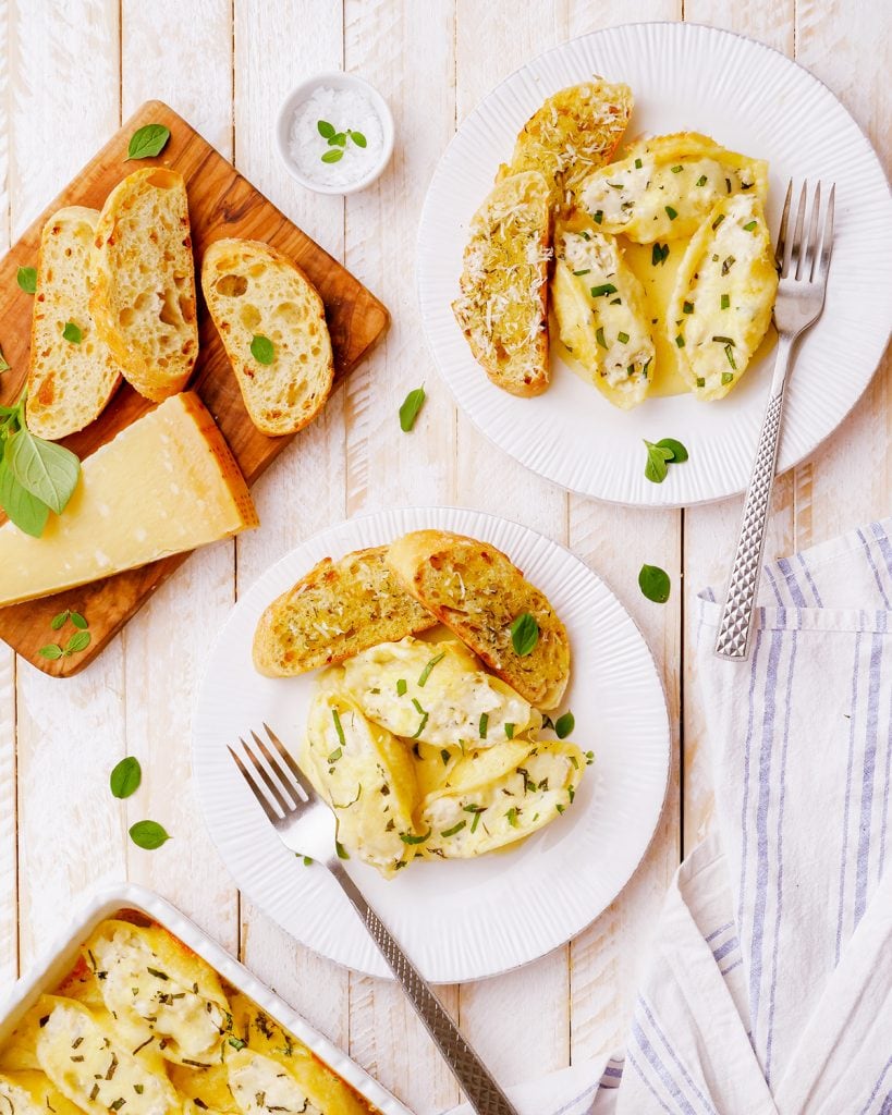 An overhead photo of two plates of chicken alfredo stuffed shells with garlic bread on them.