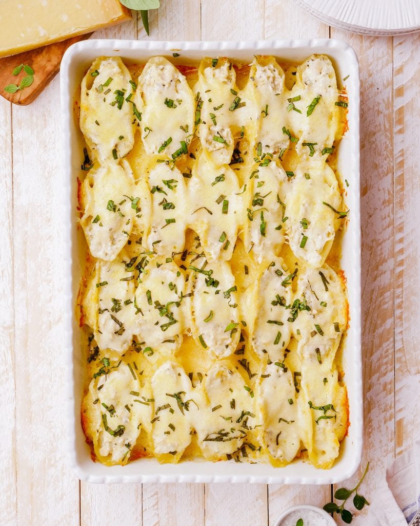 A white baking pan full of a pan of cheese covered chicken alfredo shells.