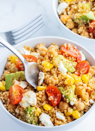 A bowl of a quinoa, chick pea, and corn salad also with tomatoes, avocado, and cotija cheese with a spoon in the bowl.