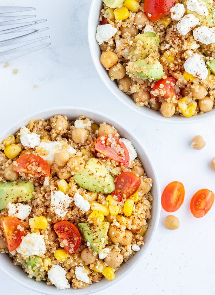 Two bowls of quinoa and corn salad topped with tomatoes, avocado, and cotija cheese.