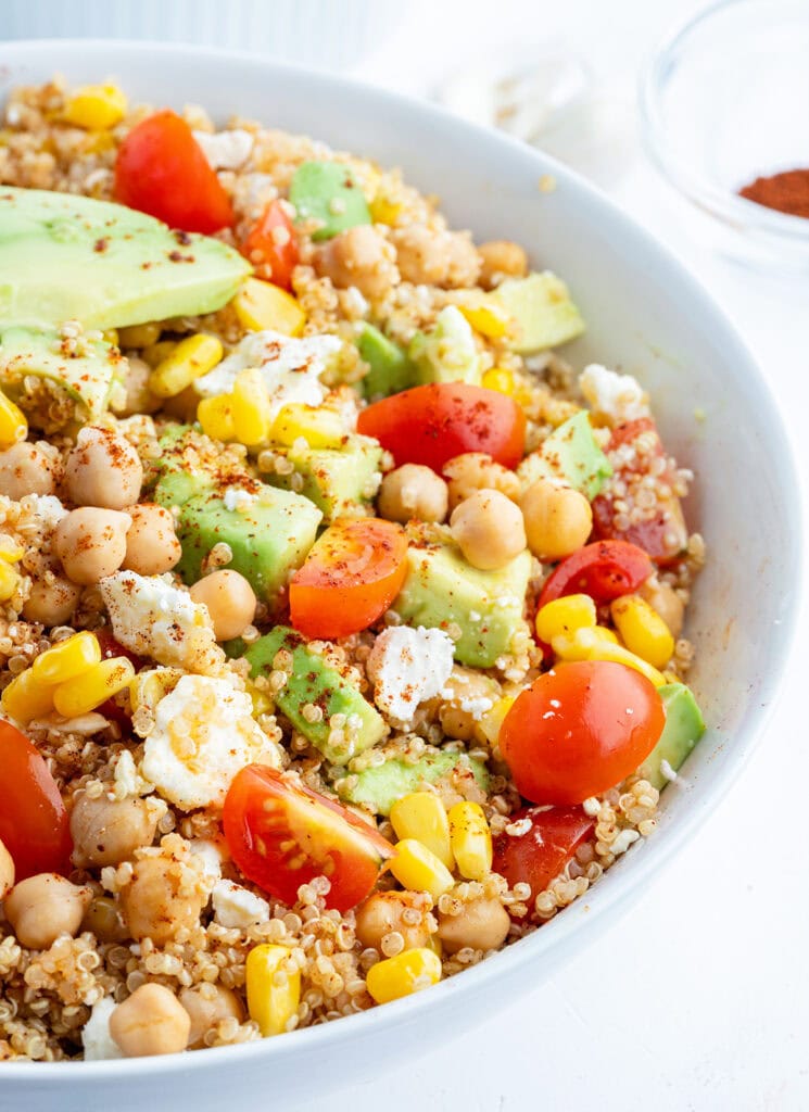 A bowl of quinoa and corn salad topped with tomatoes, avocado, and cotija cheese.