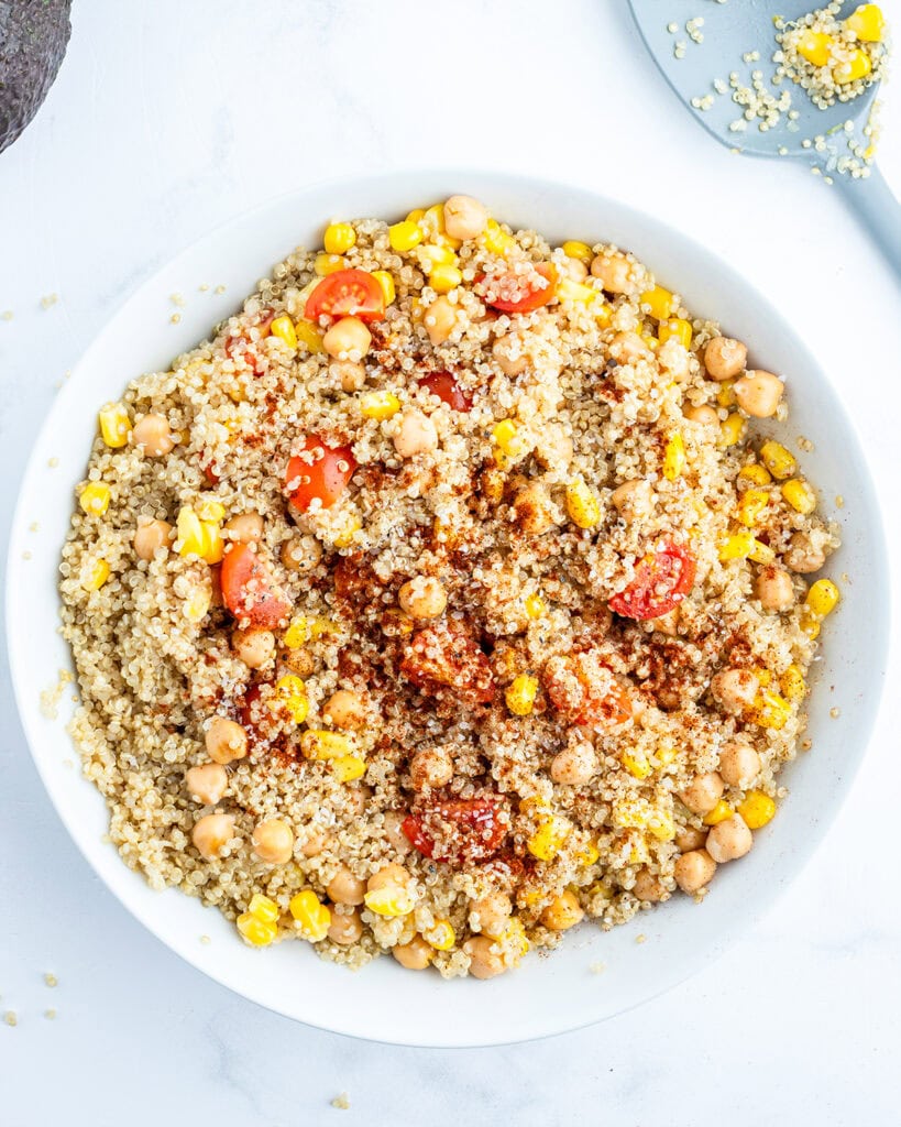 A bowl of tossed. corn, quinoa, and cherry tomatoes.