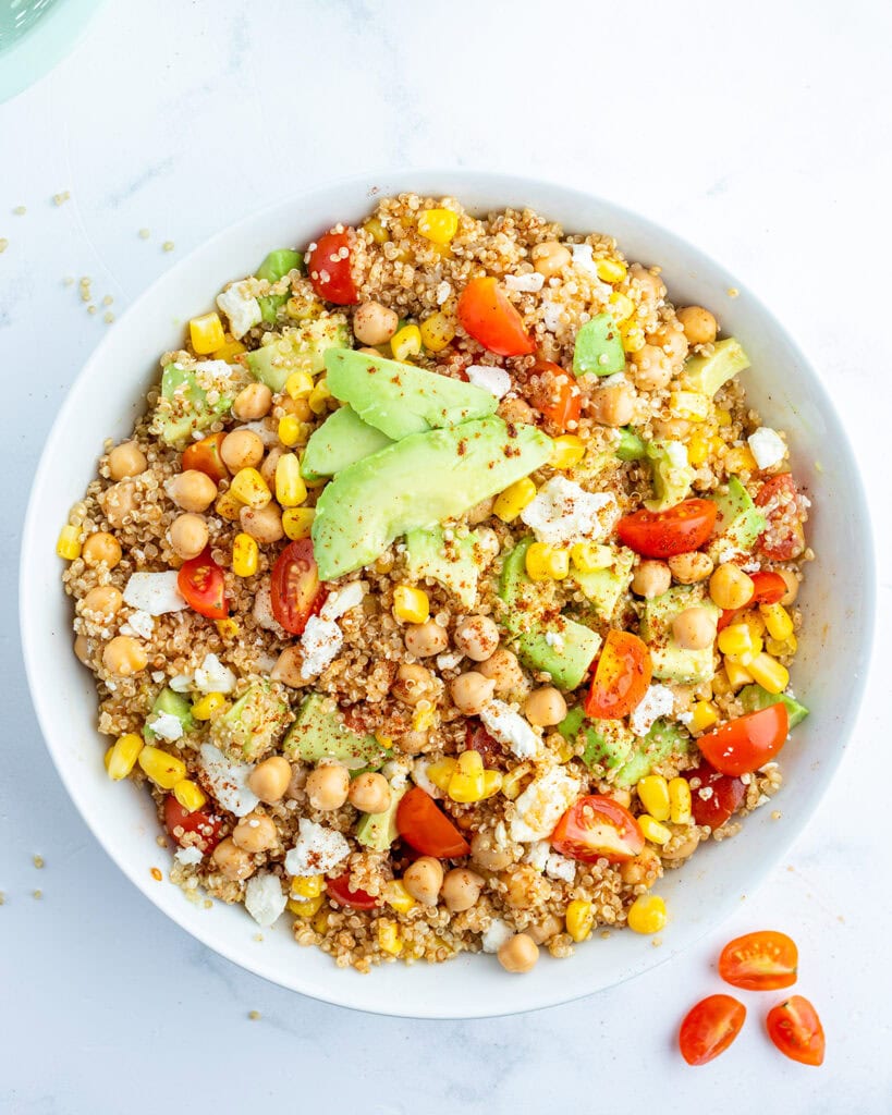 An above view of quinoa and corn salad topped with tomatoes, avocado, and cotija cheese.