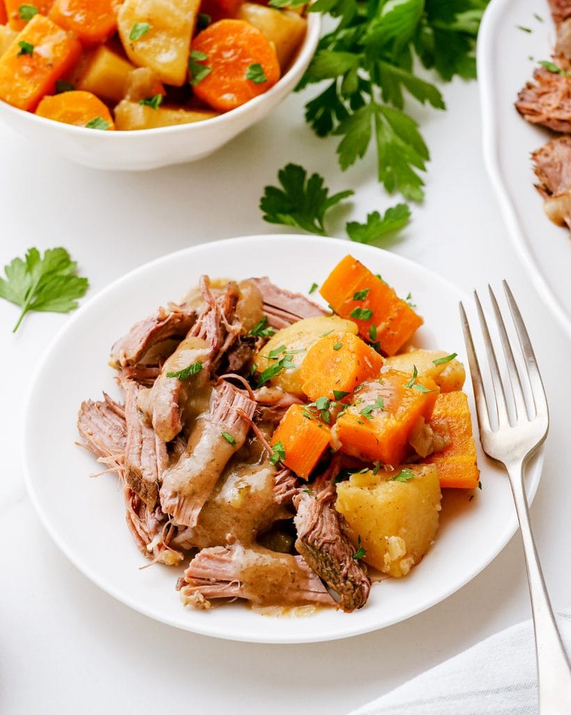 A plate of pot roast, potatoes, and carrots topped with gravy and fresh parsley.