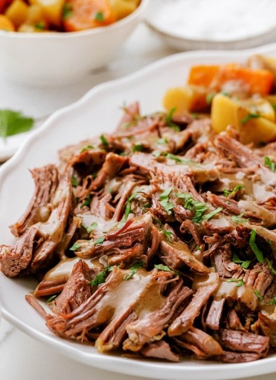 A platter full of pieces of pulled apart three envelope roast topped with gravy and fresh parsley.