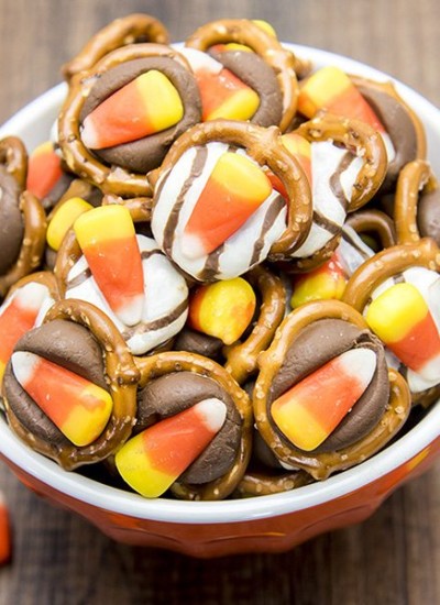 Angled view of candy corn pretzel treats in an orange bowl.