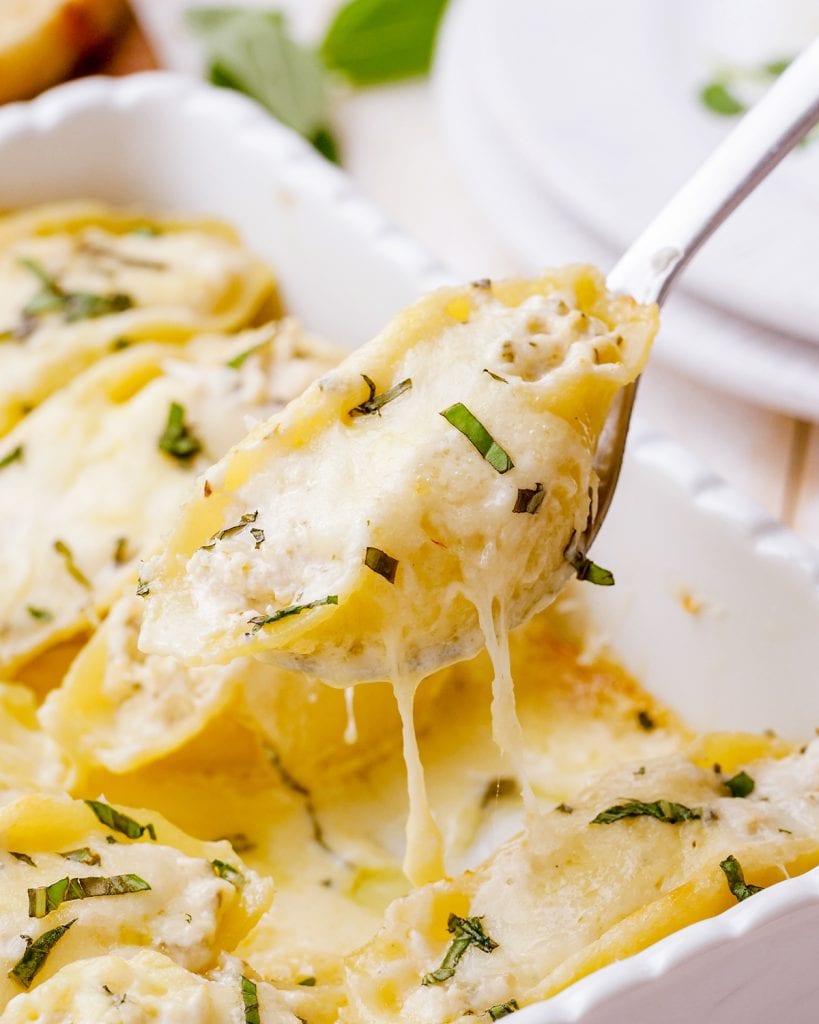 A fork lifting a cheese covered stuffed shell out of a pan of alfredo stuffed shells.