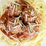 Close up view of italian meatballs on top of spaghetti on a white plate.