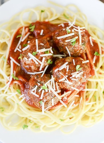 Close up view of italian meatballs on top of spaghetti on a white plate.