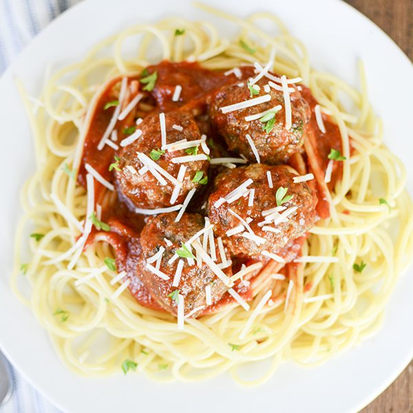 Close up view of italian meatballs on top of spaghetti on a white plate.