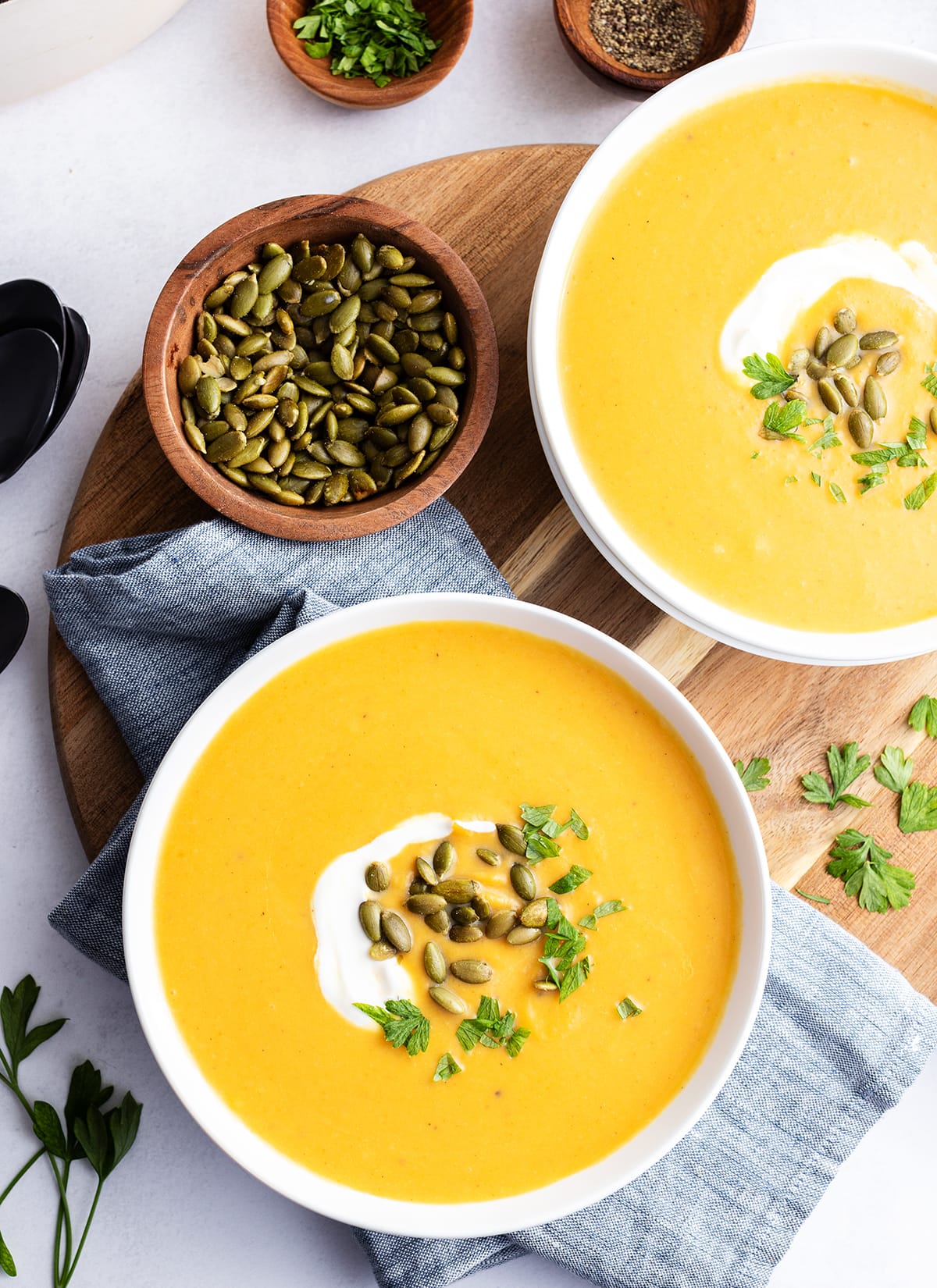 An overhead photo of two bowls of autumn squash soup. Each bowl is topped with cream and roasted pumpkin seeds.