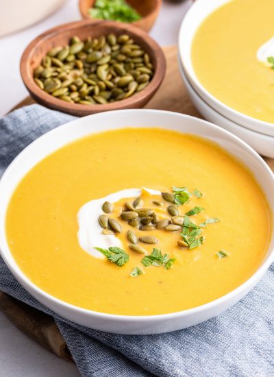 A bowl of squash soup topped with heavy cream and pepitas.