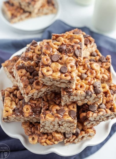 Close up image of many chocolate chip fluffernutter cheerio bars stacked on a plate in squares.