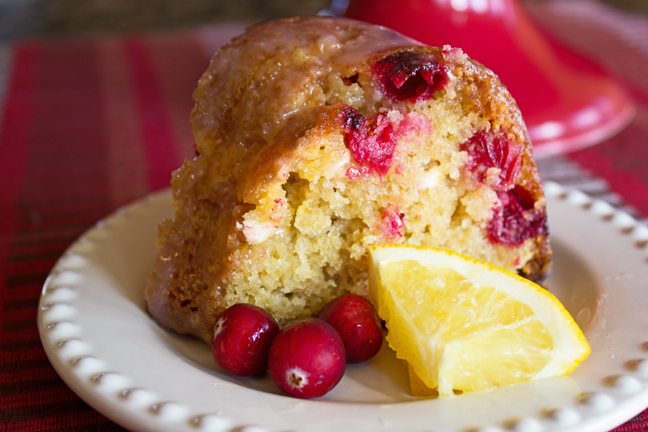 A close up of a piece of cranberry orange bundt cake with an orange wedge next to it.