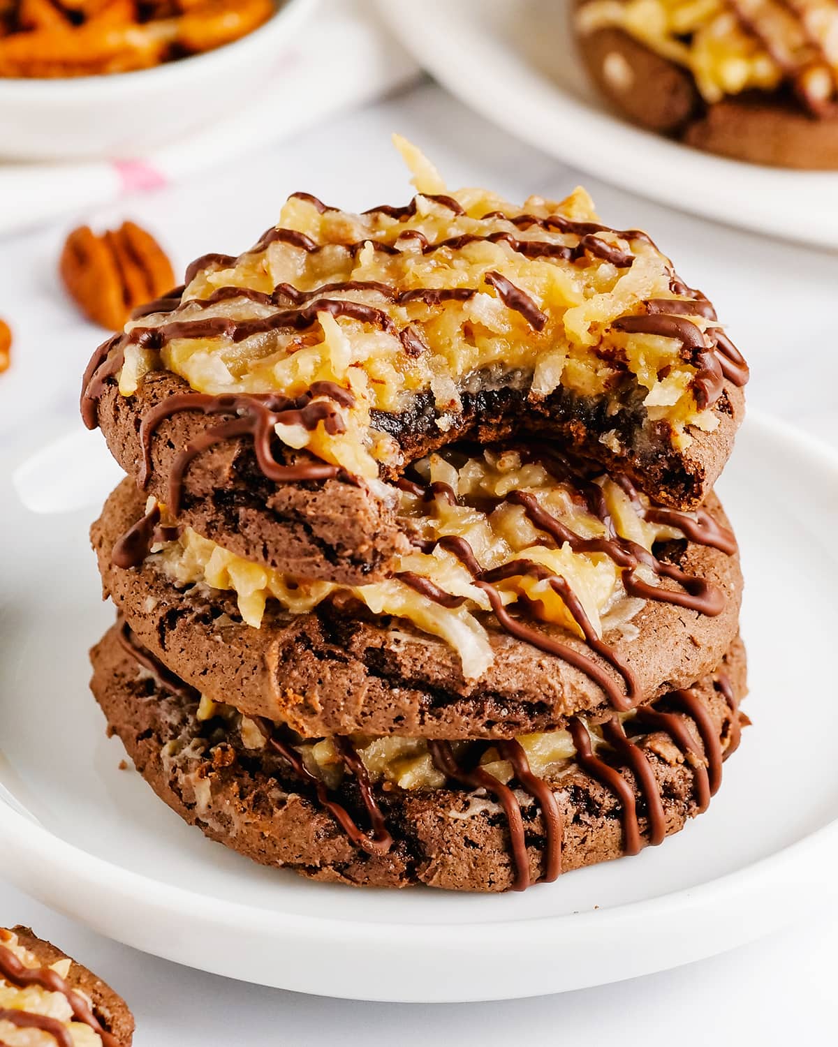 Three German Chocolate Cake Cookies stacked together with coconut pecan frosting on top, the top cookie has a bite out of it.