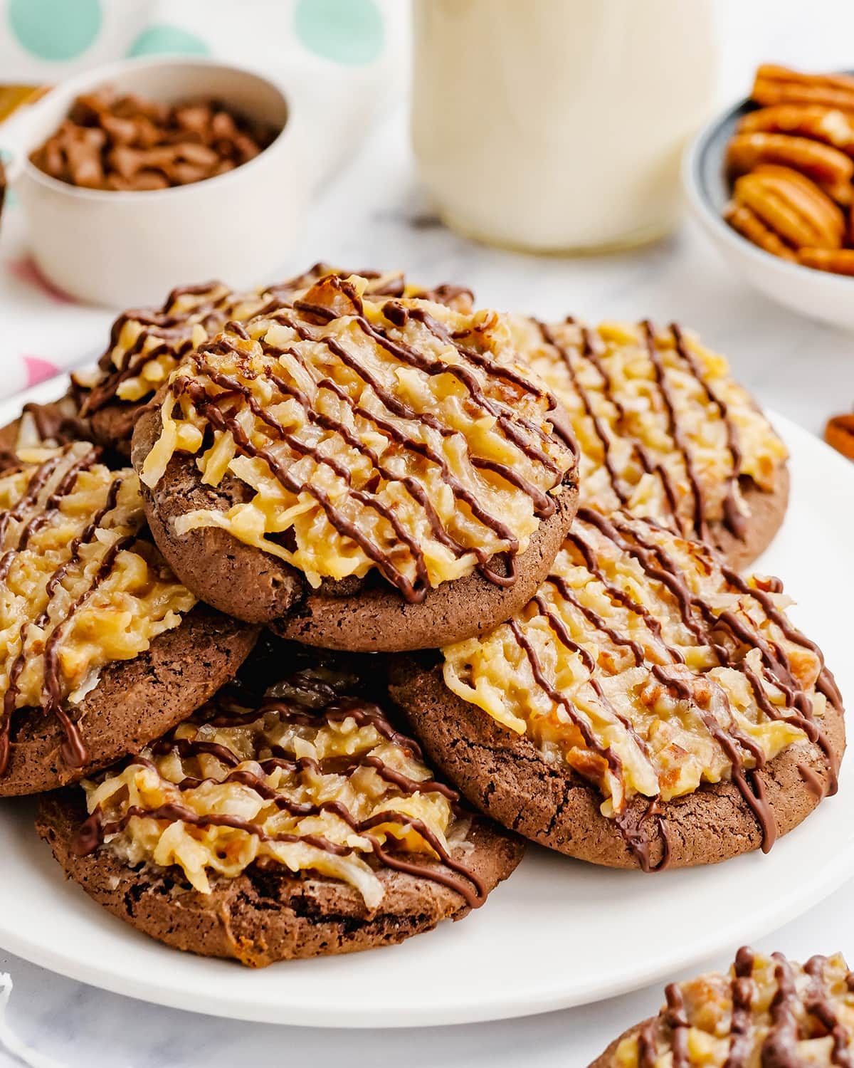 A pile of chocolate cookies topped with German chocolate coconut pecan frosting and a chocolate drizzle.