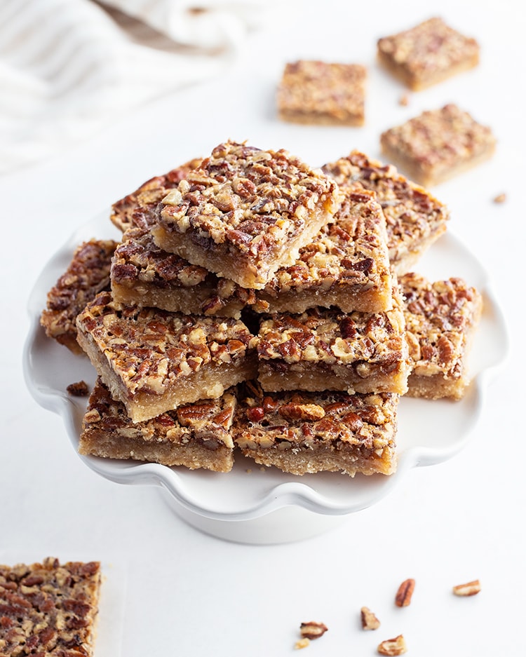 A big stack of pecan pie bars on a cake stand.