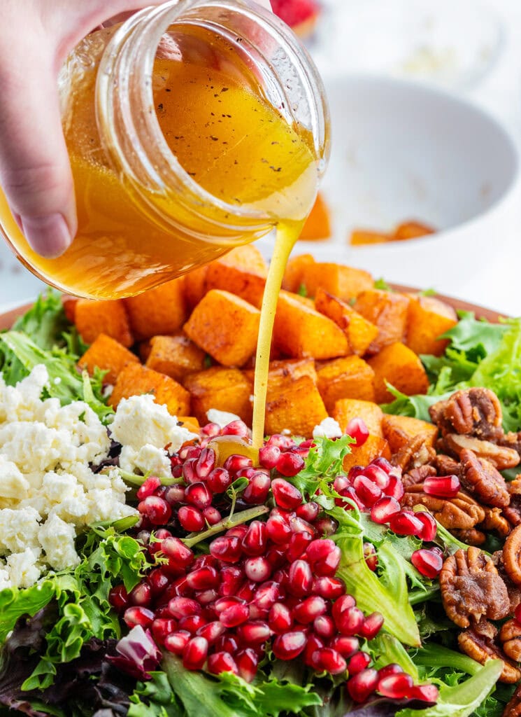 Apple Cider Vinaigrette being poured onto a fall salad with butternut squash.