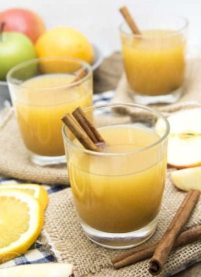 Cups of wassail with cinnamon sticks on burlap squares.