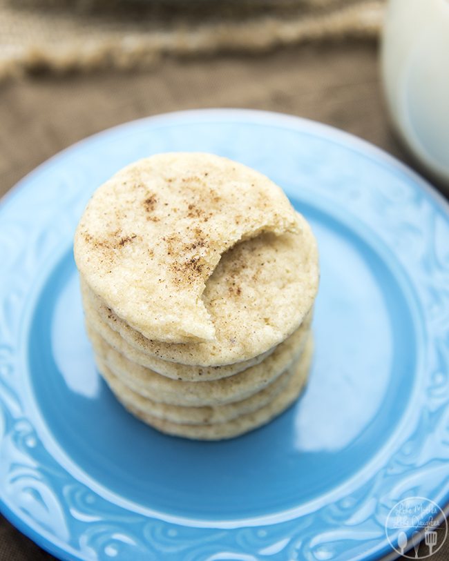 Angled view of stacked eggnog cookies on a blue plate with a cookie bite taken out.