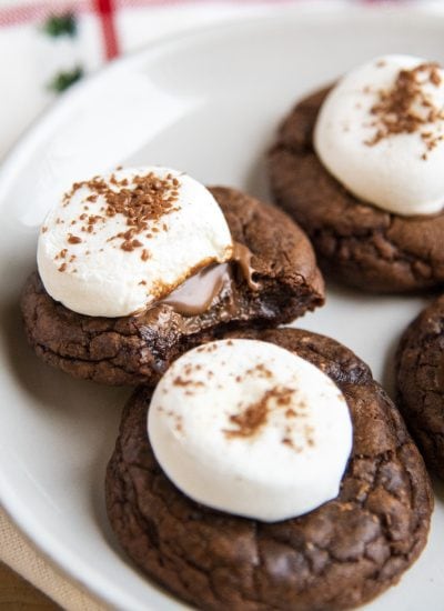 A close up of a plate of chocolate hot chocolate cookies, and one has a bite out of it.