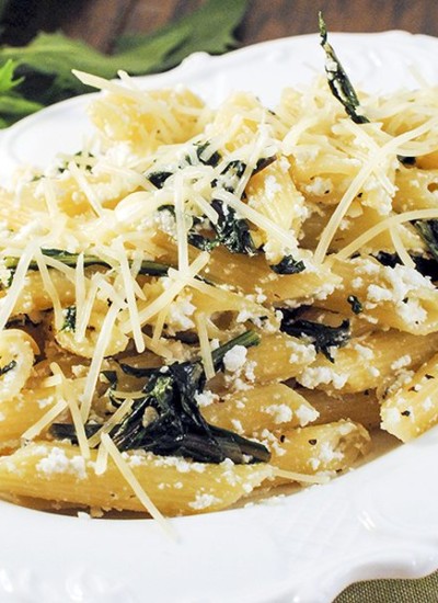 A close up of penne pasta with dandelion greens and shredded cheese on top.