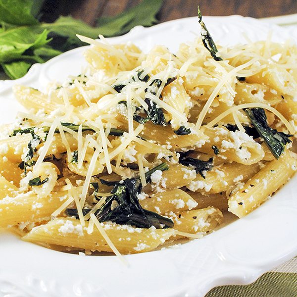 A close up of penne pasta with dandelion greens and shredded cheese on top.