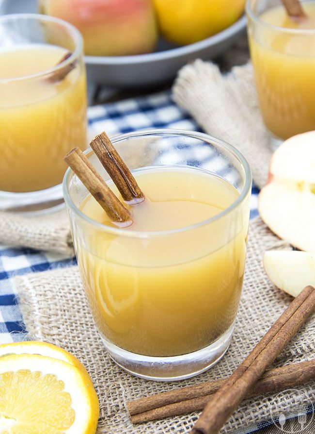 A glass of orange wassail with two cinnamon sticks in it.