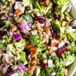 A close up of broccoli salad, with chopped broccoli, red onion, dried cranberries, sunflower seeds, and bacon, with a light creamy dressing.