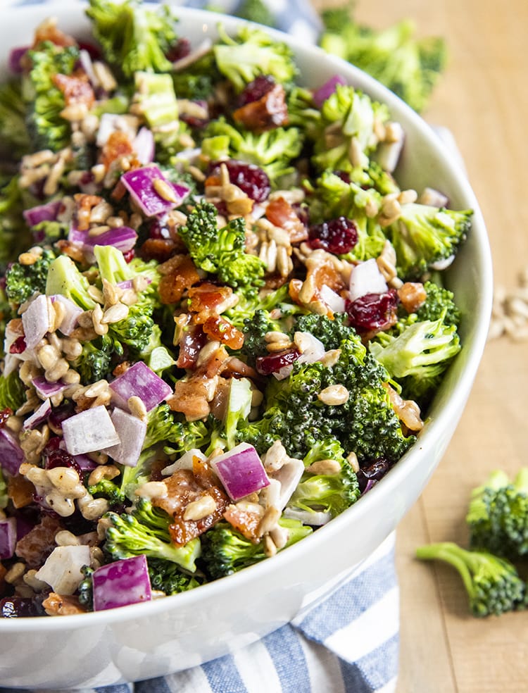 A close up of creamy broccoli salad with red onion, and bacon, in a white bowl.