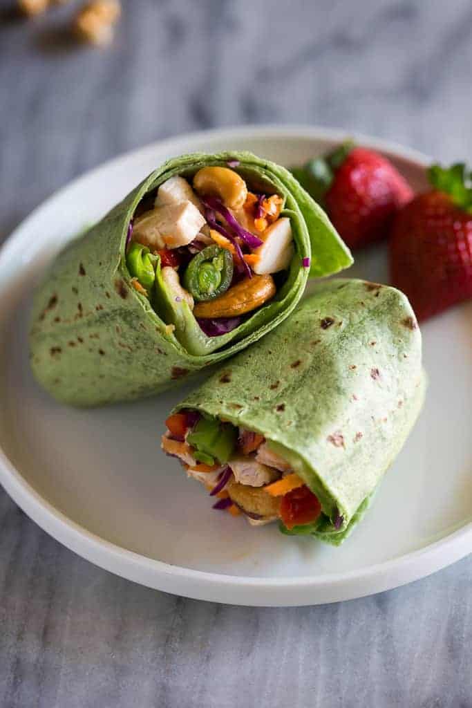 A chicken, cashew, and vegetable wrap all wrapped in a spinach tortilla and cut in half showing the filling in the middle.