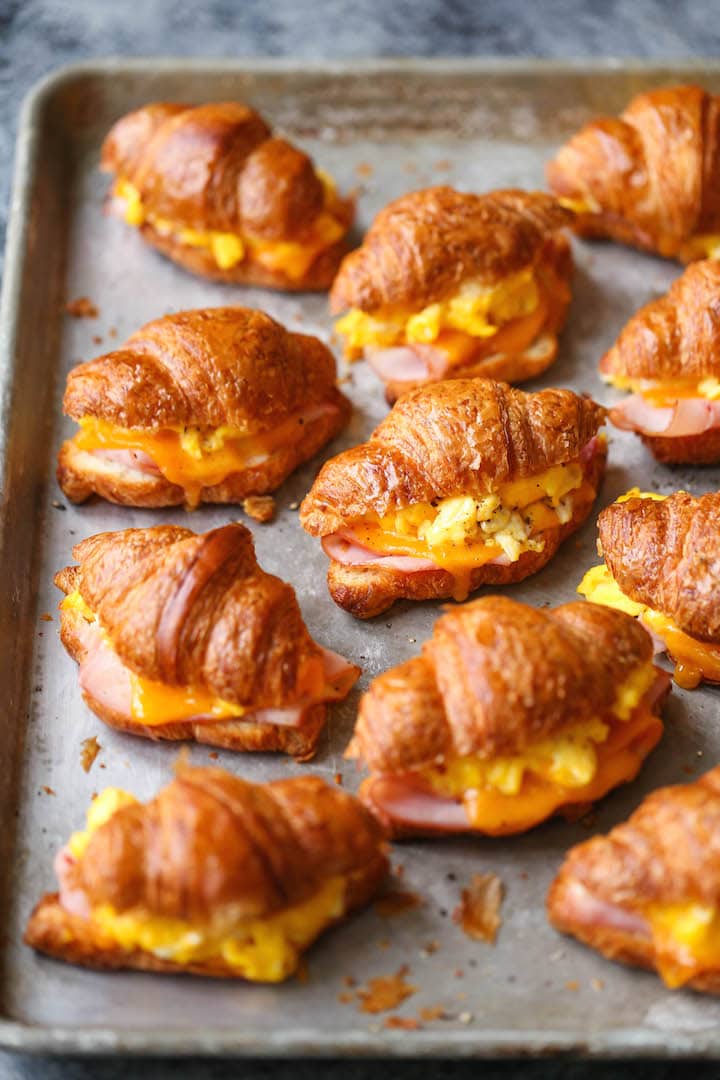 A cookie sheet loaded with croissant, ham, egg, and cheese breakfast sandwiches.