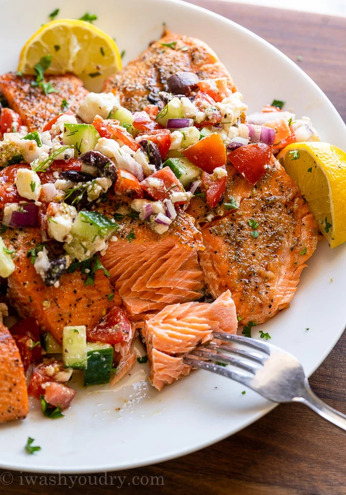 A plate of salmon filets topped with a greek salsa full of feta, cucumbers, Kalamata olives, and tomatoes.