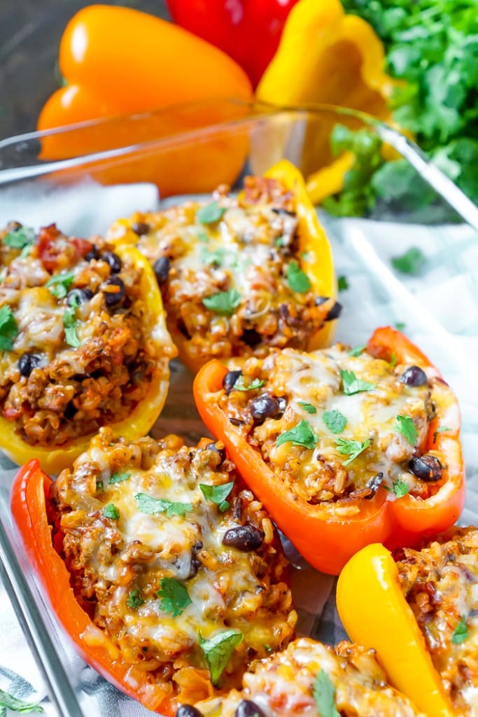 A clear baking dish full of stuffed peppers cut in half and laying down, with ground turkey in them, and topped with melted cheese.