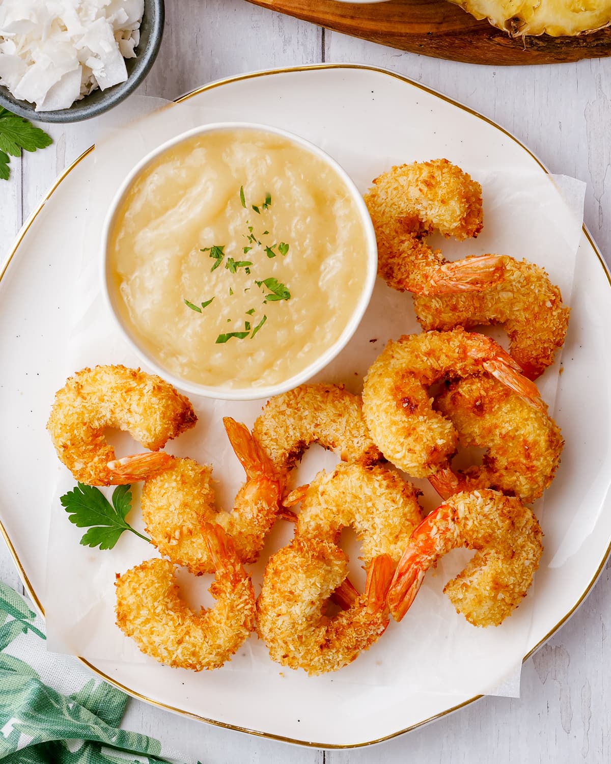 A small bowl of coconut shrimp sauce, that is a light yellow color, the bowl is on a plate surrounded by coconut shrimp.