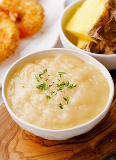 A small white bowl full of a pineapple coconut shrimp sauce with parsley sprinkled over the top.