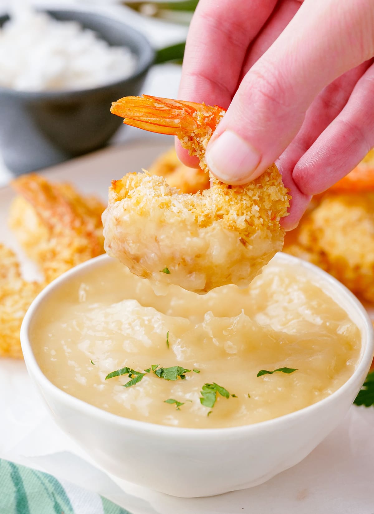 A coconut shrimp dipped into a bowl of pina colada sauce.