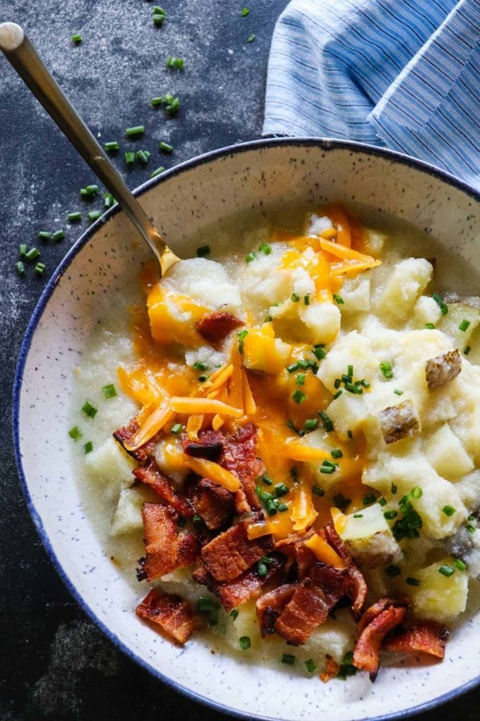A bowl of potato soup, topped with some shredded cheese and bacon pieces.