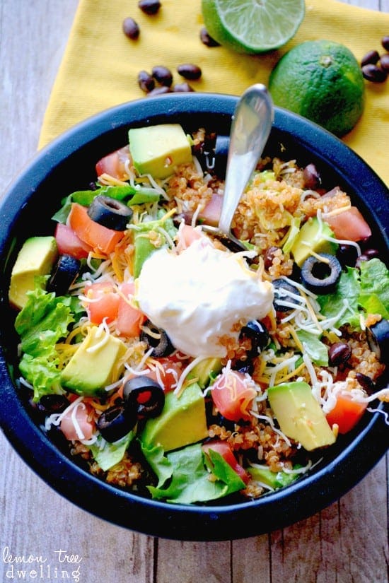 A black bowl full of quinoa, avocado pieces, diced tomato, olives, cheese, and sour cream. 