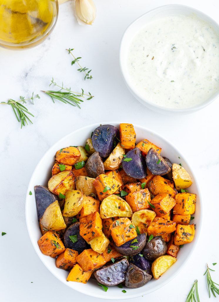 A bowl of rainbow roasted potatoes with a bowl of rosemary aioli next to it.
