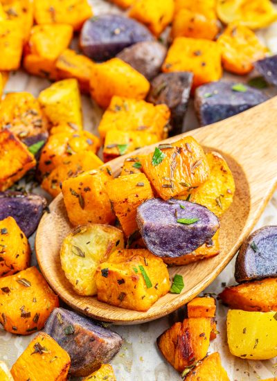 A wooden spoon topped with roasted sweet potatoes, purple potatoes, and golden potatoes.