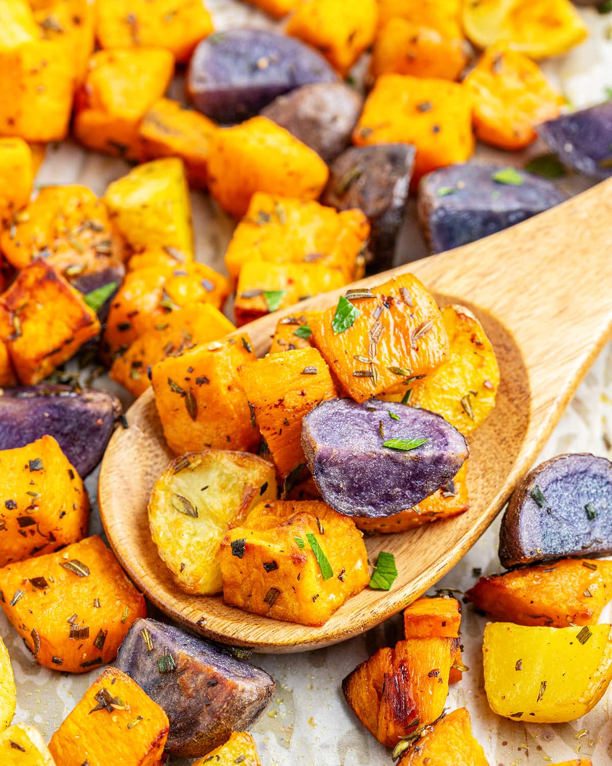 A wooden spoon topped with roasted sweet potatoes, purple potatoes, and golden potatoes.