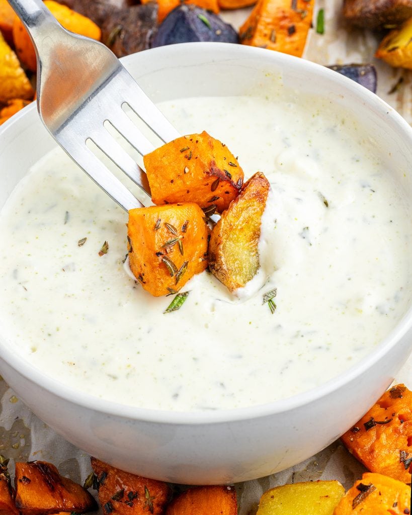 A forkful of sweet potatoes dipping into a bowl of garlic aioli sauce.